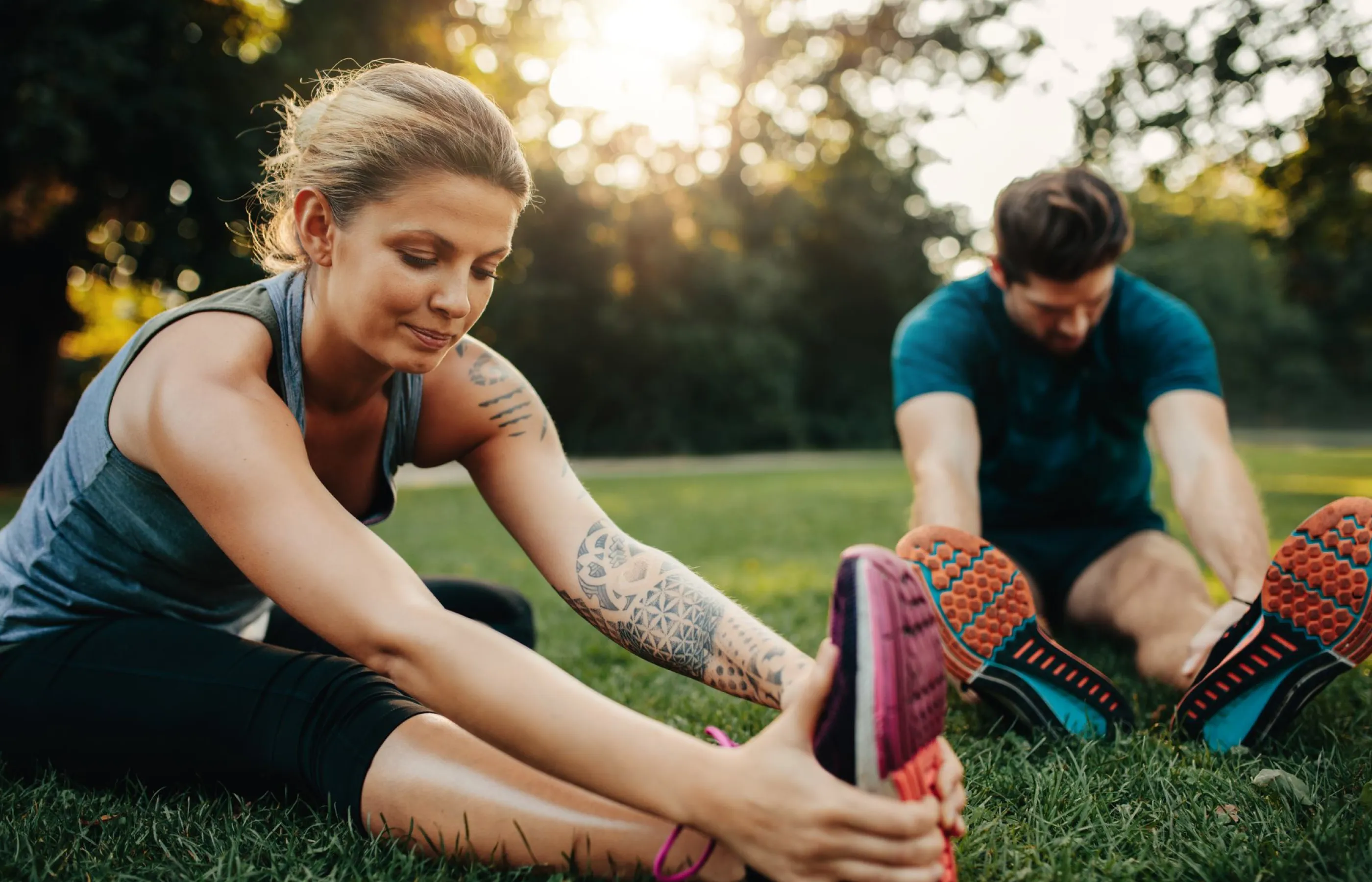 A couple is out at the park, sitting on the grass, stretching their legs. 