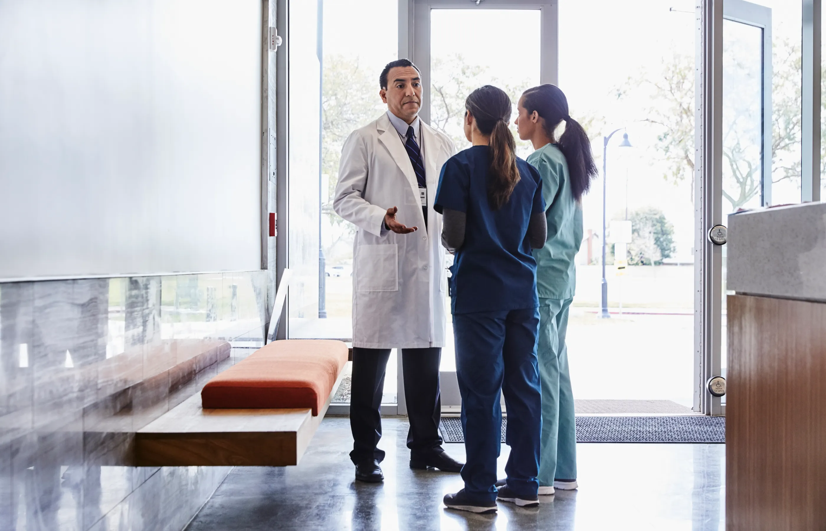 Two women, dressed in scrubs, are talking with a doctor who is wearing a lab coat. 