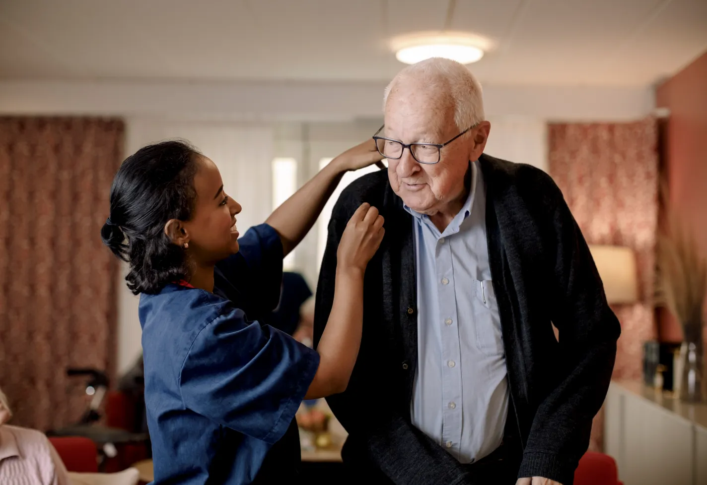 Nurse with a senior man in his home. The nurse is assisting the man as he stands. 