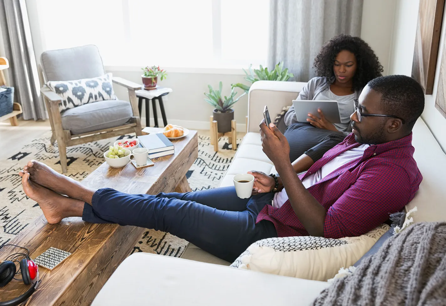 A couple is sitting on the couch as they review information individually on their phone and tablet. 