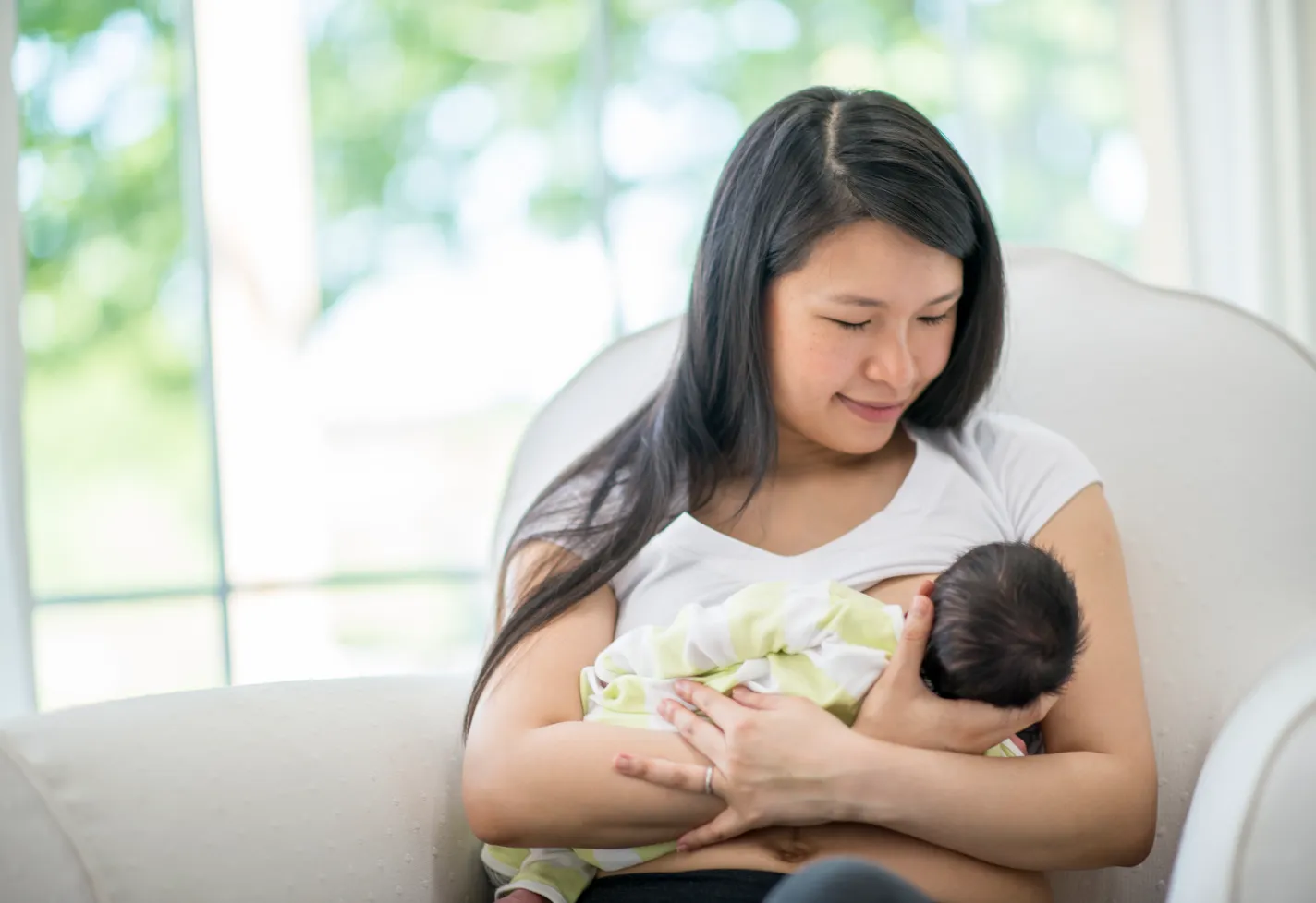 A mother breastfeeding hre baby sitting on a chair.