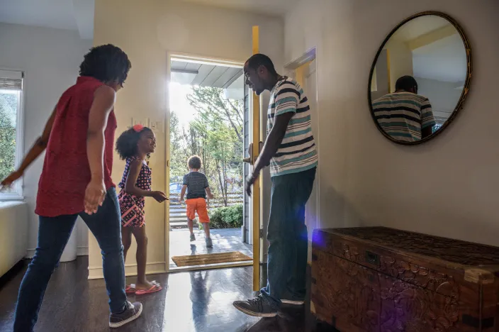 Two children and their parents are all rushing out of their front door. 