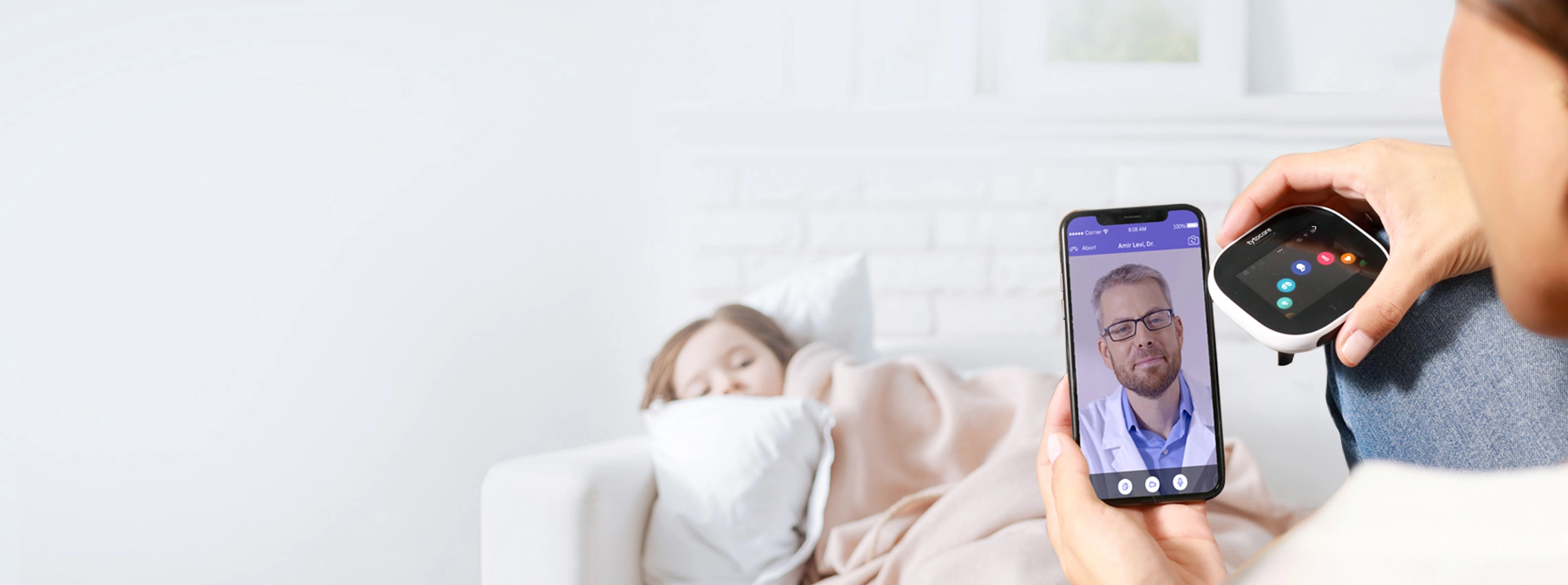 A sick child lies on a couch under a blanket and looks at their mother, who is using TytoHome to have a virtual doctor's visit